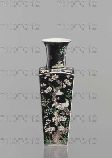 Vase, gift; Chinese art; Qing 1644–1911; 18th century; porcelain, colored famille noire; floral decorations with plum trees and birds; vessel; height 22.5 cm., A tall, narrow ceramic vase with a flared rim and a square tapering body standing against a neutral gray background; the vase has a predominantly black surface decorated with floral and foliage motifs in white, green, and pale turquoise, with branches and blossoms wrapping around the body and small bird figures perched among the branches; the rim interior is a pale off-white, and the overall finish is glossy, with subtle reflections visible at the base.
