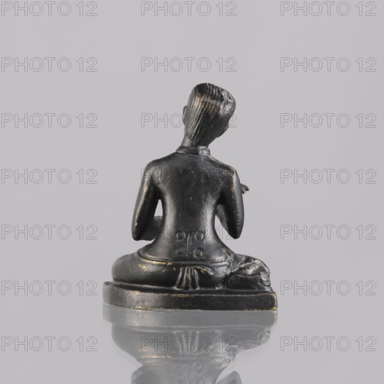 Musician figurine, Southeast Asian art, Southeast Asia culture, musicians, 1st half of the 20th century contemporary product, Cambodia place of origin, sculpture, figurine, height 6.5 cm, A small dark sculpture of a seated figure shown from the back on a flat base, with a smooth black surface and scattered spots of worn gold, the figure sitting cross-legged with arms bent at the elbows and a sculpted hairstyle with parallel grooves, the base reflecting on the glossy surface beneath, and the background a uniform light gray.