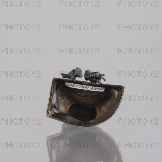 Musician figurine, Southeast Asian art, Southeast Asia culture, musicians, 1st half of the 20th century contemporary product, Cambodia place of origin, sculpture, figurine, height 6.5 cm, A small metallic object with a dark bronze and black patina sits against a pale gray background and casts a faint reflection beneath it; the object has a curved, hollow interior showing darker blackened areas and worn bronze tones, and a few small sculpted protrusions on its upper rim that are dark gray to black in color.