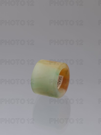 Ring, Chinese, Qing Dynasty 1644–1911, green-brown jade ornament/jewelry, 18th–19th century, origin: China; height 1.5 cm, diameter 2.0 cm., A smooth cylindrical ring-like object with a glossy surface shown against a neutral gray background and reflected faintly below; the object displays a gradient of pale green, light yellow, and warm amber tones, with slightly darker green and brownish patches and a subtle translucent quality.