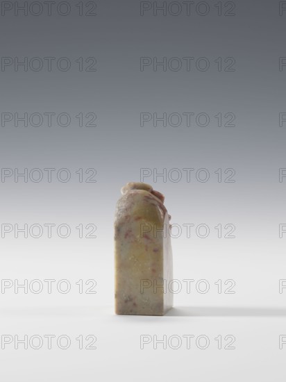 Seal stamp, Chinese, Qing dynasty 1644–1911, 19th–20th century. Seal stamp in blind, square cross-section, pendant form; decoration of cranes in bas-relief and engraving. Dimensions: height 6.9 cm, width 2.7 cm, depth 2.7 cm., A single upright rectangular block with a rounded top sits centered on a smooth white surface against a gradient gray background; the object has a marbled appearance with muted tones of beige, yellow, pink, and pale green, with a few darker flecks and subtle variations in color across its surface, and a soft shadow extending to the right.