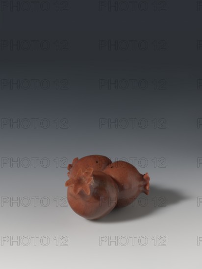 Three connected pomegranates fragment of a whole, Chinese, Qing 1644–1911, object in the shape of three connected pomegranates; each has small holes on both sides; fragment of a whole; 18th–19th century, China; sculpture; height 4.8 cm, width 8.2 cm., A group of three reddish-brown pomegranate-shaped objects sit together on a smooth surface, each with a star-shaped crown detail; the objects cast a soft gray shadow to the right and the background transitions from light gray at the bottom to dark gray at the top.