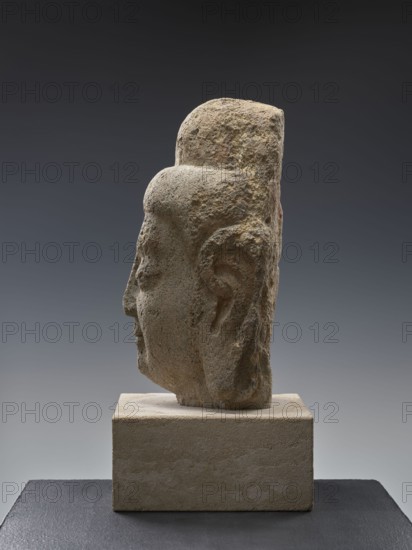 Head of Buddha, Chinese, Qing 1644–1911 and Song 960–1279 influences, Chinese Buddhism iconography; Buddha ca. 560–480 BCE with ushnisha; Song-style sculpture; 19th–20th century, China; sculpture; height 38.0 cm, A stone sculpture of a human head shown in profile, mounted on a rectangular stone base and placed on a dark surface; the head has a rounded top and a pronounced ear, with a textured, weathered surface and visible tool marks; colors visible include various shades of beige, tan, gray, and hints of brown on the sculpture and base, with a gradient gray to dark gray background.