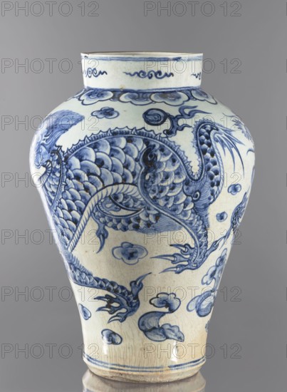 Ovoid vase with a long neck, maebyeong type Chinese: mei-ping; 18th century, Korea Joseon, 1392–1897. Porcelain vessel, height 46.0 cm, width 32.0 cm, weight 8.0 kg. Decoration: two dragons among clouds. Korean art; dragons iconography, clouds., A ceramic vase with a rounded body and narrow neck sits against a neutral gray background, decorated with an intricate blue painted design on a pale cream surface; the blue motifs include a large scaly creature with flowing limbs and claws, surrounded by cloud-like shapes and curling ornamental details, with a band of stylized wave-like patterns near the rim and a double-lined border at the base, the glaze showing subtle crackling and areas of darker blue shading and small brownish spots.