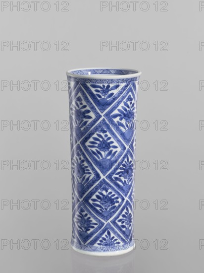 Vase, Chinese, blue-and-white porcelain, ceramics; cylindrical vessel with geometric and floral ornaments including rhombuses; 18th century China; height 23.2 cm, diameter 9.6 cm., A tall cylindrical ceramic vase with a glossy finish standing upright against a plain light gray background, decorated all over with a repeating diamond-patterned design featuring floral motifs in shades of blue on a white base, with darker blue accents along the rim and base and visible reflections on the surface.