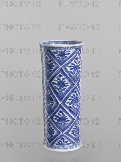 Vase, Chinese, blue-and-white porcelain ceramic cylindrical vessel with geometric and floral ornaments including rhombuses; 18th century China; height 23.2 cm, diameter 9.6 cm., A tall cylindrical ceramic vase with a glossy white base and a repeating blue geometric and floral pattern covering its surface, showing diamond-shaped panels each containing stylized blue flowers and leaves, a narrow patterned rim and base, and visible colors of blue and white against a neutral gray background.