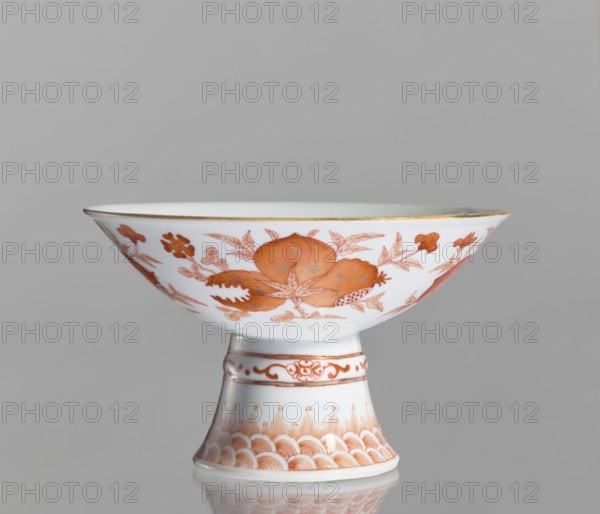 Platter, Chinese, ceramics; porcelain platter on a tall, widening foot. Decoration painted with red overglaze iron: inside center centripetal composition a peach, pomegranate, and Buddha's hand; outside three flowered branches with peach fruit, pomegranate fruit, and a Buddha's hand, a sign of happiness surrounded by four bats; ornamental bands on the foot. White glaze. 19th century, China. Vessel; height 11.7 cm, diameter 19.5 cm., A white ceramic stem bowl with a flared shallow dish atop a tapered foot, decorated with orange floral and fruit motifs and fine orange border patterns, with a thin gold rim at the dish edge, shown against a plain light gray background.