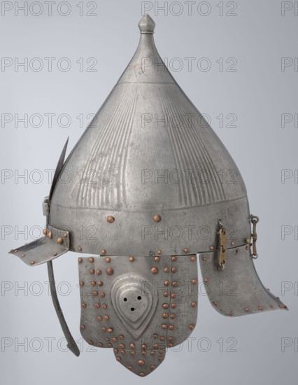 Helmet, creator unknown, Turkish, Ottoman dynasty 1299–1922, 16th century. Ottoman militaria headgear with movable cheekpieces and a nosepiece passing through the browband. Fluted bell. Browband and cheekpieces connected with copper rivets; neckpiece additionally with brass hinges. Materials: metal; weight 1.92 kg; height 39.0 cm, width 37.0 cm, depth 24.0 cm., A conical metal helmet with a pointed top and flared base, shown in shades of silver and gray with visible vertical ribbed patterns on the dome; the helmet has attached overlapping neck and cheek guards with rounded edges and a few decorative raised ridges, all secured by several round copper-colored rivets; a narrow metal bar curves downward at one side and a small hinged clasp with a brass-toned plate is visible on the other side, and the surface shows areas of slight wear and subtle darkening.