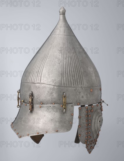 Helmet, Ottoman dynasty 1299–1922, Turkish, Islamic art; 16th century, Turkey. Militaria headgear with movable cheekpieces and a nosepiece passing through the browband. Fluted bell. Browband and cheekpieces connected with copper rivets; neckpiece additionally hinged with brass. Weight 1.92 kg; height 39.0 cm; width 37.0 cm; depth 24.0 cm., A metal pointed helmet with a conical top and a small finial, showing a textured surface with vertical ridges and a weathered patina in shades of silver and gray, featuring a flared brim and attached cheek and neck guards secured with a group of small copper-colored rivets and a few brass-colored fittings and chain links, all set against a pale gray background.