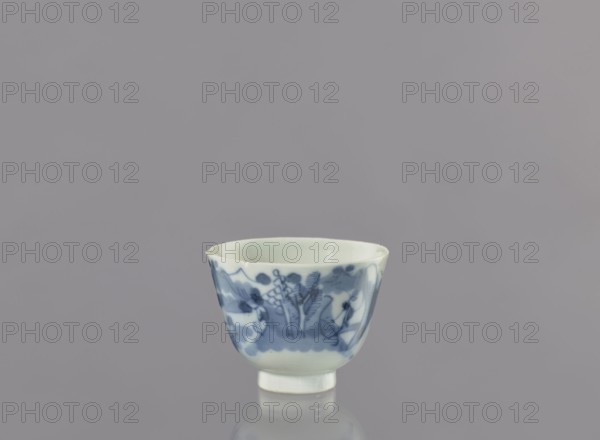 Bowl, Japanese, ceramics, bowl with landscape motifs, ca. 1750–1800, Japan, vessel; height 6.3 cm, diameter 8.3 cm, A small porcelain cup with a flared rim and short foot sits centered against a smooth gray background, the cup showing a white base color with blue painted decorative motifs around its exterior, including organic shapes and floral-like patterns; the interior appears pale and glossy, and the surface of the cup reflects subtly on the glossy surface beneath it.