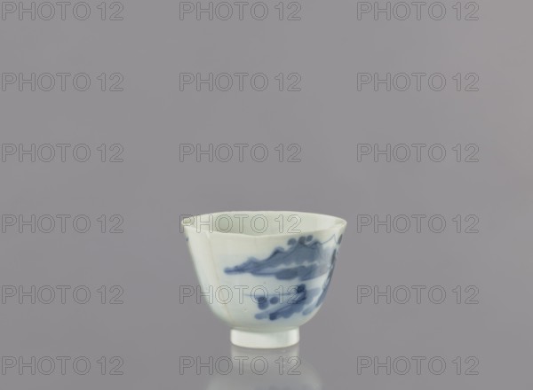 Bowl, Japanese, landscape motifs, ceramics, ca. 1750–1800, Japan, vessel, height 6.3 cm, diameter 8.3 cm, A small porcelain cup sits centered against a smooth gray background; the cup is white with blue painted brushstroke patterns around its exterior, with a slightly flared rim and a short, round foot, and the surface shows faint glazing reflections and subtle hairline variations in the white; visible colors include gray, white, and blue.