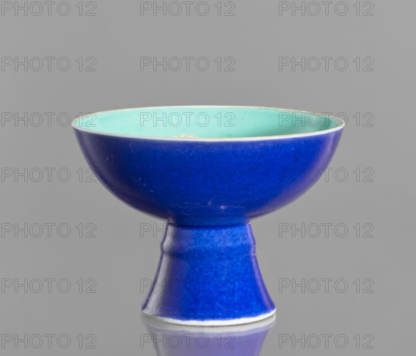 A porcelain footed bowl on a high foot, Chinese, 19th century Qing Dynasty. Cobalt blue exterior glaze, green interior glaze; overglaze iron hieroglyphs, overglaze enamel paints, gilded edge and gilt decoration. Height 12 cm; diameter 16.9 cm., A ceramic chalice-like bowl with a glossy deep blue exterior and a pale turquoise interior, sitting on a matching deep blue pedestal base; the surface shows subtle variations in glaze texture and small scuffs, and the object is reflected faintly on the neutral gray background beneath it.