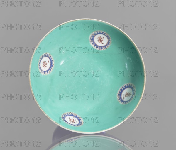 A footed porcelain bowl, Chinese, 19th century Qing Dynasty. Cobalt blue exterior glaze, green interior glaze; overglaze iron hieroglyphs, overglaze enamel paints, gilded edge and medal-gilding. Decorative vessel, height 12 cm, diameter 16.9 cm., and provenance. Categories: footed bowls, ceramics, colored porcelain, glazed ceramics., A shallow round dish with a smooth turquoise interior and a thin off-white rim, decorated with a few round medallions placed near the edge that have blue scalloped borders and white centers, resting on a reflective gray surface with a soft gray background; visible colors include turquoise, blue, white, off-white, and gray.