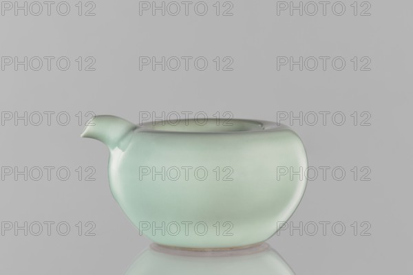 Water vessel, Chinese, Qing dynasty Kangxi period, 1662–1722, ceramic celadon decorative vessel with celadon glaze, signed. China. Height 6.5 cm; width 11.7 cm., A smooth, rounded ceramic vessel with a short spout on one side sits centered against a plain backdrop; the vessel displays a soft pale green color with subtle gradients and a glossy finish, and a faint reflection of the vessel appears below it on the surface.
