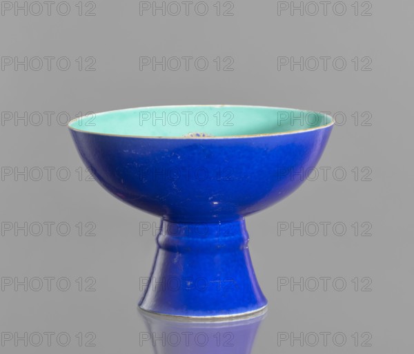 A tall footed porcelain bowl, Chinese, glazed ceramics with outer cobalt-stained glaze and green inner glaze. Decorated with overglaze iron hieroglyphs, overglaze enamel paints, and gilding with a gilded edge. 19th century Qing Dynasty. Vessel, height 11.8 cm, diameter 16.8 cm. Maker, provenance unknown. Classification: footed bowl, decorative vessel, colored porcelain., A glossy pedestal bowl with an exterior in vibrant blue and an interior in pale turquoise resting on a flared foot, shown against a plain gray background; the bowl has a smooth rounded rim with a thin metallic edge and displays minor surface scratches and reflections.