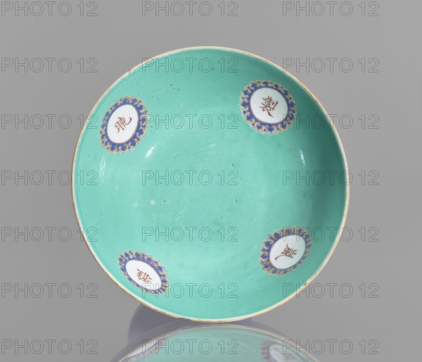 A tall footed porcelain bowl, Chinese, glazed ceramics with stained cobalt outer glaze and green inner glaze. Overglaze iron hieroglyphs, overglaze enamel paints, gilding with a gilded edge. 19th century Qing Dynasty. Vessel, height 11.8 cm, diameter 16.8 cm. Maker, provenance unknown., A shallow round bowl with a smooth turquoise interior and a thin gold rim, decorated with a few circular medallions around the inner wall that feature white centers and ornate blue and gold scalloped borders; the background behind the bowl is gray and the bowl casts a faint reflection below it.