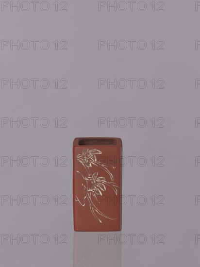 Vessel, Japanese, engraved decorations, ceramics, flowers iconography, Red-brown stoneware with engraved decoration dyed white with engobe, 19th century, Japan, vessel; height 11.1 cm, width 6.3 cm, depth 6.3 cm, A rectangular reddish-brown ceramic container with an open top sits centered against a muted gray-purple background, showing a faint reflection beneath it; the front face of the container features an etched floral design in a light contrasting color with flowing curved lines and stylized leaves, and the top interior appears darker brown.