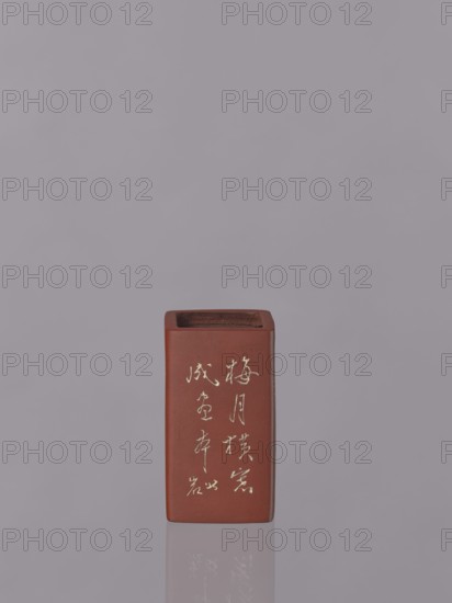 Vessel, Japanese art, Japanese culture, engraved decorations, ceramics, flowers iconography, red-brown stoneware with engraved decoration, dyed white with engobe, 19th century, Japan, vessel, height 11.1 cm, width 6.3 cm, depth 6.3 cm, A rectangular reddish-brown ceramic vessel with an open top stands on a reflective surface against a soft gray background; the vessel shows a vertical arrangement of light-colored markings on its front face and a darker interior rim visible at the top, and its reflection appears faintly below it.