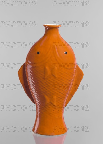 Vase in the shape of two fish; creator, Chinese; Qing dynasty 1644–1911; ceramics; decorative vessel; fish motif; red and white glaze; 19th century; China; height 35.8 cm, An orange ceramic object shaped like a stylized fish with a narrow neck and flared rim is centered against a light gray background; the fish form shows textured scale patterns and raised fins, with two small dark circular spots suggesting eyes, glossy reflections on the orange surface, and a small portion of a pale underside visible at the rim and base.