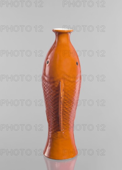 Vase in the shape of two fish, Chinese, Qing dynasty 1644–1911, ceramic decorative vessel with red and white glaze, 19th century, China; height 35.8 cm, An upright ceramic object shaped like a fish with a narrow neck and flared rim, glazed in bright orange with a glossy finish; the surface shows textured scale-like patterns on the body and smooth areas near the head, with small dark circular spots where the eyes would be; the base is slightly flared and rests on a reflective surface, and the background is a uniform light gray.