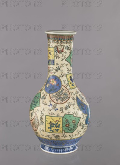Vase, Japanese, Meiji 1868–1912, ca. 1870–1880; colored porcelain with cloisonné enamel; decorated with insects and butterflies, floral decorations and geometric ornaments; Nagoya, Japan; vessel; height 39.5 cm, diameter 20.5 cm., A narrow-necked ceramic vase with a bulbous body standing against a plain gray background, decorated overall with a cream-colored ground patterned with a network of fine black floral sprigs and dotted details, containing a patchwork of shaped panels and roundels in colors including blue, green, yellow, red, and pink, each panel containing floral and butterfly motifs and small decorative elements, the neck bordered at the rim by a band of red and green geometric motifs and a thin brown lip, the lower body set above a wide blue band with stylized vine decoration and a white foot rim with blue accents.