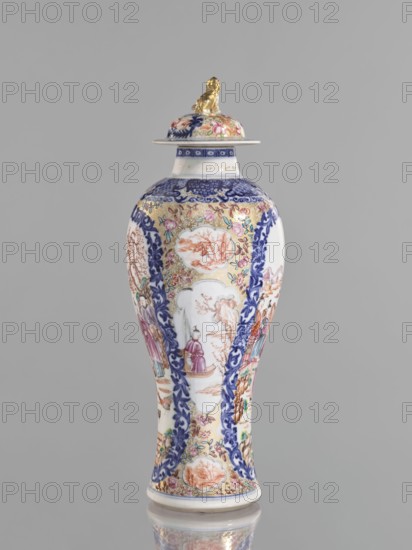Vase with a lid, Chinese, 18th century. Porcelain vessel height 28 cm with white glaze, underglaze cobalt painting and overglaze enamels in sepia, black, iron red, and gold. Lid topped by a modeled seated lion. Decoration: geometric and plant ornament around the neck; two large reserves bordered with plant ornament containing figural scenes in a landscape, two smaller reserves with figures in a landscape; background of twigs with flowers on a gold ornamental ground. Genre scenes, floral decorations, and lions. Provenance unknown., A tall vase with a lid stands against a plain gray background, featuring ornate painted decoration in colors including white, blue, gold, pink, green, purple, and orange, with a small gold sculpted figure perched on the lid; the vase body tapers from a rounded shoulder into a narrow waist and flares slightly at the base, showing panels of floral patterns, scrolling blue borders, and several painted scenes with human figures and landscape motifs, and the lid a...