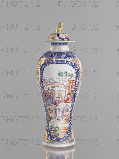 Vase with a lid, Chinese, ceramics, colored porcelain, 18th century. Vessel height 28 cm. The lid is topped with a modeled seated lion. Decoration: geometric and plant ornament around the neck; two large reserves bordered with plant ornament filled with figural scenes in a landscape, two smaller reserves with figures in a landscape; background of twigs with flowers on a gold ornamental ground. White glaze, underglaze painted with cobalt; overglaze enamels in sepia, black, iron red, and gold. Provenance unknown., A tall porcelain vase with a lid is shown against a plain gray background; the vase has a predominantly white body with extensive blue decorative borders and ornate painted scenes featuring people in traditional clothing and architectural elements, with additional colors including gold, pink, green, red, and purple; the lid is topped by a small gold-colored figurine and decorated with similar multicolored patterns; the vase sits on a reflective surface that mirrors its base.
