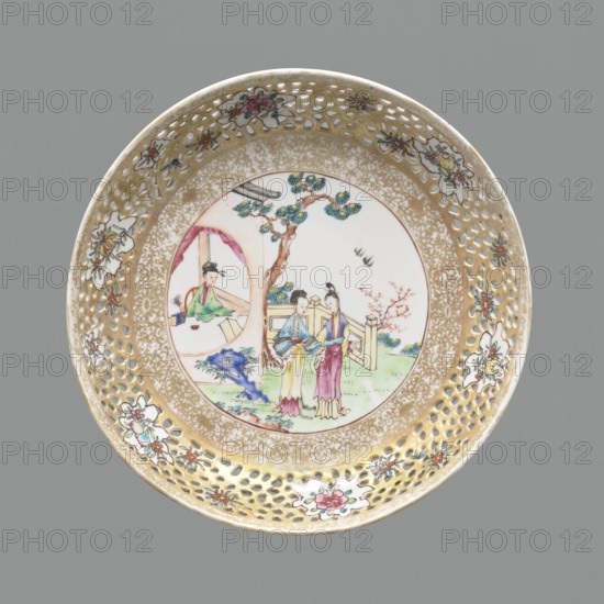 Plate, Chinese, figural scenes, openwork, colored porcelain, ceramics, plant ornaments, Qing 1644–1911. Openwork rim with plant projections flowers, fruits. White glaze. 18th–19th century, China. Vessel; height 3.5 cm, diameter 20.8 cm., A round decorative ceramic plate with a perforated rim and a painted central scene; the rim has a gold background with a pattern of small cutout holes and several floral motifs in white, pink, red, green, and blue, and the inner border shows a speckled gold design. The central round panel displays a courtyard scene with a tree in brown and green, a few figures wearing garments in pastel colors including yellow, pink, blue, green, and purple, and a small building element with a circular opening painted in muted tones; there is also a blue rock-like form, some grassy areas in green, and a small flowering branch in pink. The overall background behind the plate is gray.