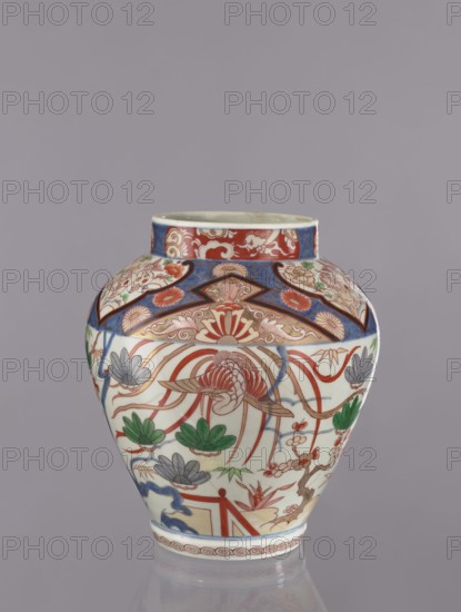 Vase tsubo, Japanese, Imari studio, ca. 1720–1740, Arita, Japan. Colored porcelain ceramics decorated with phoenixes, flowers, pine trees, geometric and plant ornaments. Vessel; height 28.5 cm., A rounded ceramic vase with a short neck sits against a plain gray background, decorated with intricate painted designs in red, blue, green, and gray. The upper band of the vase shows a patterned border with red and blue sections and floral motifs, while the main body features stylized floral and foliage elements, including large petal-like forms and leafy clusters in green and gray, along with flowing red ribbon-like lines. Additional decorative panels in blue and red frame fan-shaped and scalloped motifs, and a narrow repeating border encircles the base. The overall surface is glossy and the colors are vivid against the light-colored ceramic.