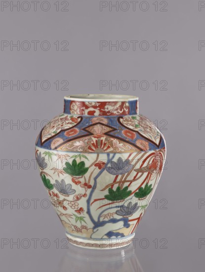Vase tsubo, Japanese, ca. 1720–1740, Arita, Japan. Colored porcelain Imari tsubo decorated with phoenixes, flowers, pine trees, plant and geometric ornaments; vessel height 28.5 cm., The image shows a rounded ceramic vase with a short neck against a plain gray background. The vase is decorated with painted floral and botanical motifs in colors including red, green, blue, purple, and white, with areas of darker blue and touches of yellow. The upper section features ornate red and blue patterned bands and stylized floral medallions, while the body displays a repeating arrangement of leaves and flowers in green and purple with red stems and accents. A wavy blue element runs vertically among the floral designs, and the base has a decorative border with a repeating circular motif in red. The surface appears glossy and reflective.