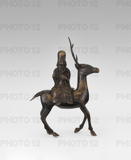 Shoulao on a deer - incense burner, unknown sculptor, deer, figurines, Chinese art, Chinese culture, restitution provenance, incense burner, sage, Taoism, longevity shou iconography, Shouxing iconography, Chinese symbols, Qing 1644–1911, 18th century, China, sculpture, height 27.5 cm, A small dark metallic sculpture shows a seated elderly figure with a long beard and high rounded headwear riding a slender deer with tall branching antlers; the figure wears layered flowing robes and holds its hands near its chest, and both the rider and the deer display worn golden highlights on a predominantly dark brown surface, with the deer's body elongated and its legs poised as if walking against a light gray background.