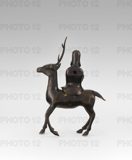 Shoulao on a deer - incense burner, unknown sculptor, deer figurine depicting Shoulao Shouxing, Taoist sage of longevity; bronze sculpture, Qing dynasty 18th century, China; height 27.5 cm., A dark bronze sculptural figure of an animal with slender legs and a raised tail supporting a seated humanlike form on its back; the animal has a long neck, an elongated head with a visible snout, and a single prominent antler with branching points; the seated figure is simplified with a smooth rounded head and a rounded torso that features a circular hole on its back; the surfaces show patches of lighter brown and golden worn areas against the overall dark brown and black tones; the scene is set against a pale neutral background.