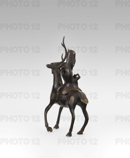 Shoulao on a deer - incense burner, deer figurine; Chinese art, Taoist sage Shoulao Shouxing iconography representing longevity; Qing dynasty 18th century, China; sculpture; height 27.5 cm; incense burner., A small dark brown sculptural figure of an animal resembling a deer with slender legs and upward-curving antlers, carrying a seated humanlike figure on its back; the sculpture shows smooth rounded forms and worn lighter brown highlights on raised areas, with visible contours of the animal’s body, the rider’s head and torso, and the animal’s tail; the background is a smooth pale gray to white gradient.