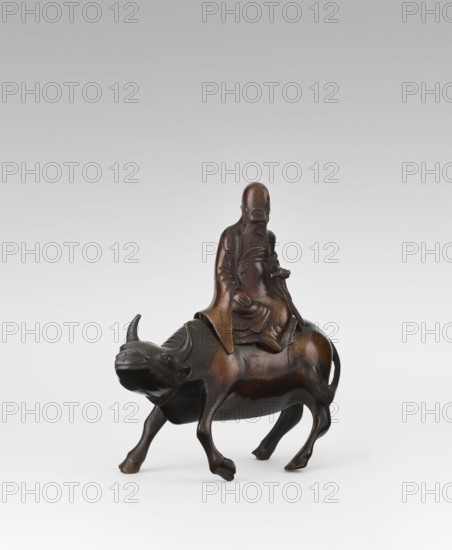 Shoulao on a buffalo — incense burner; creator unknown, Chinese; subject: Shoulao Shouxing seated on a buffalo with male figures; Taoist iconography; material: sculpture/figurine used as an incense burner; date: Qing dynasty 1644–1911, 19th century; place of origin: China; dimensions: height 20.7 cm, width 20.7 cm., A dark brown carved figure of an elderly person with a long beard seated on the back of a water buffalo; the person wears a flowing robe and has hands resting near the lap and on the buffalo, with a calm facial expression. The buffalo has a rounded body, curved horns, and four legs positioned as if walking, with a slightly raised tail. The surface shows variations of dark brown and lighter brown highlights giving a polished wooden appearance against a plain light gray to white gradient background.