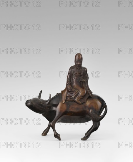 Shoulao on a buffalo — incense burner; maker, Chinese; men; buffaloes; Taoism; incense burner depicting a sage Shouxing; Qing dynasty 1644–1911, 19th century; sculpture/figurine; height 20.7 cm, width 20.7 cm, A dark brown carved figure of a bearded man wearing flowing robes seated on the back of a water buffalo, the buffalo shown in a walking pose with curved horns and a slightly raised tail, the man holding a small object in his hand and with detailed facial features and folds in his clothing, set against a pale gray background with visible color tones of dark brown, lighter brown highlights, and gray.
