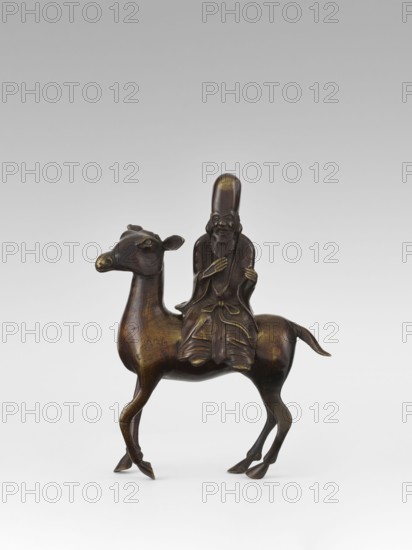 Shoulao on a deer - incense burner, unknown sculptor, deer, Chinese art, Chinese culture, restitution provenance, Taoism, incense burners, Shouxing iconography, sages, Qing 1644–1911, 18th century, China, sculpture, height 23.7 cm, A small bronze sculpture depicting a robed figure seated on the back of an animal that resembles a deer or camel, the figure wearing a tall rounded hat and a long flowing robe with visible folds, a beard and a calm facial expression, the animal shown standing with slender legs and slightly raised hooves and a gently curved tail, the surface showing a patina with dark brown and golden highlights, set against a light gray to white gradient background.