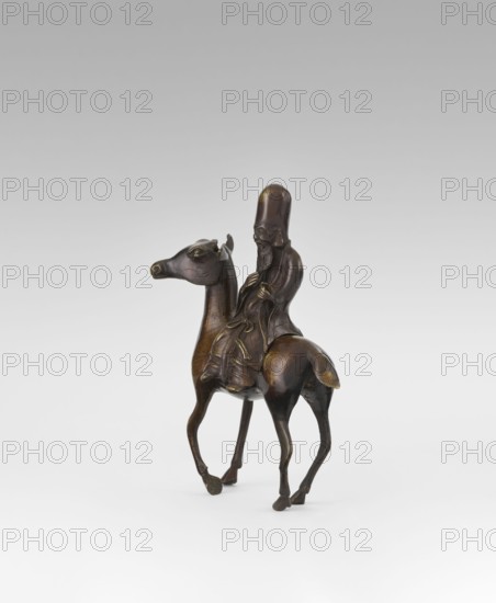 Shoulao on a deer - incense burner, unknown sculptor, deer, Chinese art, Chinese culture, Taoism, incense burner depicting Shouxing iconography, sages, Qing 1644–1911, 18th century, China, sculpture, height 23.7 cm, A small bronze-colored sculpture shows a robed figure with an elongated rounded head seated on the back of a slim, long-legged animal resembling a horse or camel; the figure has a detailed beard and holds flowing garments that drape over the animal's back, and the animal has a pronounced muzzle and upright ears; the surface of the objects shows darker brown and subtle golden highlights, and the background is a smooth gradient of light gray to white.