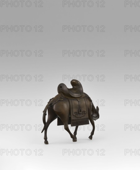 Mule with saddle - incense burner, Qing style, Chinese art, Chinese culture, mules, animals, saddle cloths, saddles, Qing 1644–1911, 19th century, China, incense burner, height 16.8 cm, A small bronze sculpture of an animal viewed from behind and slightly to one side, with a curved saddle on its back and a decorative blanket draped over its body; the animal has slender legs, a long tail that hangs down and curves, and a lowered head with visible ears and a short horn; the surface shows smooth, worn bronze tones with darker and lighter brown variations, and the background is a gradient of light gray to white.