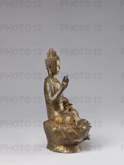 Buddha on a Lotus Throne, Chinese, Chinese art, figurine, Chinese Buddhism, lotus throne iconography, Buddhist art, Qing 1644–1911, ushnisha, natural patina, 19th century, China, sculpture, height 28.5 cm, A metallic sculpture of a seated figure with a textured hair bun and elongated earlobes sits on a stylized base resembling a lotus. The figure is shown in profile with one hand raised and the other resting near the lap, wearing a draped garment with visible folds. The surface shows worn and flaking areas revealing patches of gold and darker metallic tones, along with spots of greenish patina. The background is a smooth neutral gray, and the base sits on a lighter gray surface.