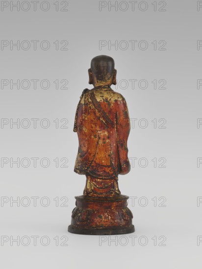 Monk, unknown role classification of creator, craftsman author; Chinese; Luohan iconography; arhat iconography; sages, monks; Buddhist art; lotus throne iconography; sculpture, figurine; Qing 1644–1911, 19th century; China; height 24.7 cm, A small standing figurine viewed from behind on a round tiered base, with a rounded head and visible ears, draped in a long robe that falls to the base; the surface shows worn areas and flaking. The visible colors include red, gold, black, brown, and a little dark green.