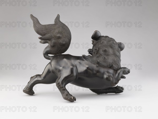 Censer — lion; maker, Chinese; Qing dynasty 1644–1911; ceremonial/ritual vessel; iconography: lion fo; small lion that forms the cover is most likely missing; 19th century, China; censer; height 28.5 cm, width 17.7 cm., A dark bronze sculptural animal shown in profile on a light neutral background, with a glossy, smooth body and textured mane and tail featuring concentric circular patterns; the creature has a rounded head with small rounded ears, a slightly open mouth, and a curled, ornate tail raised upward; its limbs are muscular and positioned as if in motion, with sculpted paws and small raised details on the legs; visible colors include dark brown to black on the sculpture and light gray to off-white in the background.
