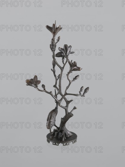 Candlestick shokudai, Japanese, magnolias, Meiji 1868–1912, candlesticks, plant tendril, cranes iconography, 2nd half of the 19th century, Japan, candlestick, height 49.5 cm, A dark bronze-colored metal sculpture of a tree-like branch with several blossoms and buds, mounted on a round base with decorative cutouts, showing a bird perched near the lower trunk; colors visible include dark brown, bronze, and hints of black against a pale gray background.