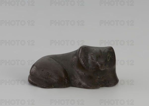 Paperweight, — Asian raccoon dog tanuki; maker, Chinese; Qing dynasty 1644–1911, 19th century; sculpture/figurine; materials: paperweight; subject: raccoon dog/dog; dimensions: height 1.9 cm, width 4.45 cm, depth 2.7 cm; provenance unknown., A small dark brown sculpted object in the shape of a reclining animal is centered against a pale gray background, showing a smooth rounded body with subtle carved details suggesting facial features and limbs, with a few areas of darker and slightly greenish patina and a few shallow decorative markings on its surface.