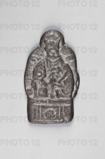 Thogcha with a representation of a human figure; maker, Himalayan Tibetan Buddhist art; amulet/cult object; sculpture/figurine; human figures; Tibet; 18th–1st half of the 20th century : height 4.7 cm, width 2.8 cm., A small sculpted object placed on a light gray background showing a single rounded-top figure in a darker gray metallic color with a slightly reflective surface; the figure appears to have a textured, relief-like front with carved shapes suggesting a head and an upper body, surrounded by an outer contoured border and resting on a rectangular base that has incised decorative panels, all rendered in shades of dark gray and silvery gray against the pale gray backdrop.