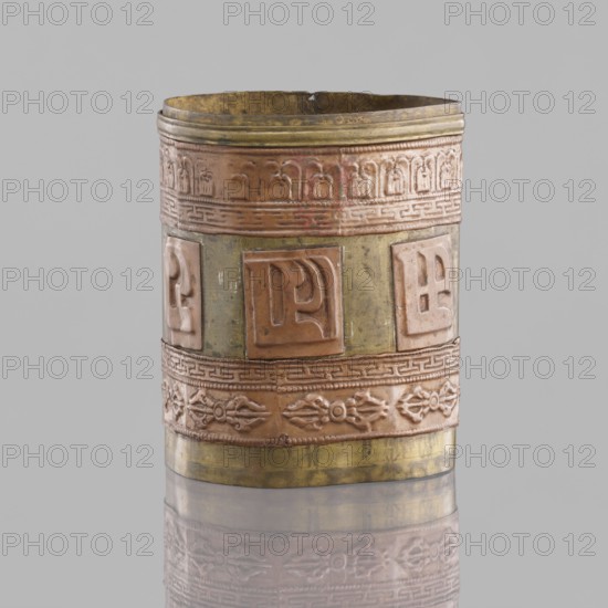 Cylinder, craft, Tibetan, inscribed, vajras, applied copper sheet, 19th century, Mongolia, Tibet, varia, length 7.3 cm, diameter 6.0 cm, A cylindrical metal object standing upright with a slightly uneven rim and a reflective base showing its faint mirror image, featuring bands of raised decorative panels and repeating embossed motifs; the surface shows a mix of warm copper tones and muted greenish-brass areas, with hints of darker tarnish and subtle brownish patina.