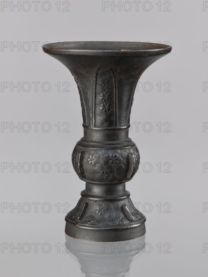 Gu-type vase gu cup, gu cups, Chinese art, Chinese culture, ceremonial/ritual vessel with spiral and plant motifs, Qing dynasty 1644–1911, 18th century, China place of origin ?, vessel; height 14.0 cm, diameter 10.0 cm, A dark metallic vase with a flared rim and a narrow waist stands against a light gray background, showing a textured surface with decorative raised patterns including spirals and floral motifs, a rounded bulbous midsection, a slightly flared foot, and subtle variations of black and dark gray with hints of brown patina.