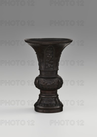 Gu-type vessel, gu cup, Chinese, ritual/ceremonial vessel, Qing dynasty 1644–1911, 18th century, China; maker, height 15 cm, diameter 10.7 cm., A tall, dark brown vase with a wide flared rim and a narrow waist rising from a rounded, bulbous midsection to a textured base, featuring raised decorative panels and carved swirling motifs; the surface appears aged with subtle variations in brown and black tones, set against a smooth gray background that fades from darker at the top to lighter toward the bottom.