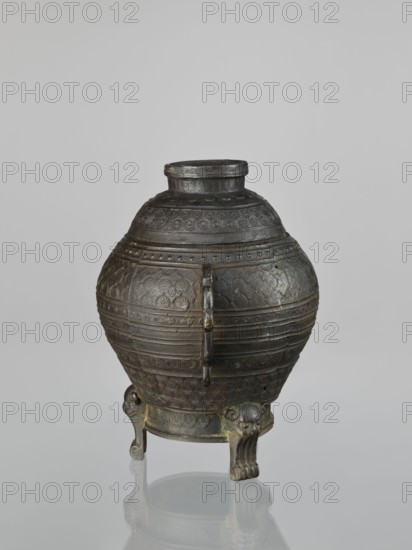 Dui-type vessel with a lid, censers, ritual/ceremonial vessel, Dui form; materials and maker, Chinese, Qing dynasty 1644–1911, possibly 19th century; decorative motifs include meander ornament, leiwen, geometric patterns, lion iconography; height 26.5 cm, width 26.5 cm., A rounded metal vessel with a short cylindrical neck sits on a reflective surface, showing a dark patina of gray and brown with hints of greenish corrosion; the body is decorated with several bands of repeating geometric and circular embossed patterns and horizontal ridges, and a vertical strap-like element runs down the front; the vessel rests on a small round base supported by three short tripod legs each carved with stylized animal faces and paw-like feet in darker gray and bronze tones, and the background is a smooth light gray.