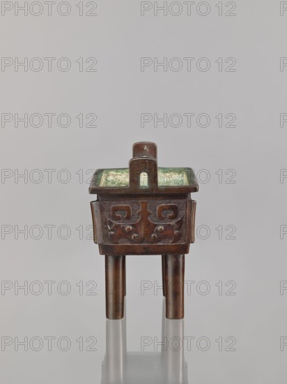 Fangding incense burner, Narozno Eckersdorf, Chinese art; fangding vessel; Chinese; ceremonial/ritual vessel with meander and leiwen ornament and taotie iconography; Qing dynasty 1644–1911; 18th century; bronze vessel standing on four cylindrical legs; height 15.3 cm, width 13.1 cm, depth 10.3 cm, A small rectangular bronze vessel with a square rim and a handle rising from its center sits on three cylindrical legs; the exterior shows carved decorative motifs on its sides while the interior has a greenish patina, and the object displays colors of brown, green, and a hint of bluish oxidation against a pale gray background.