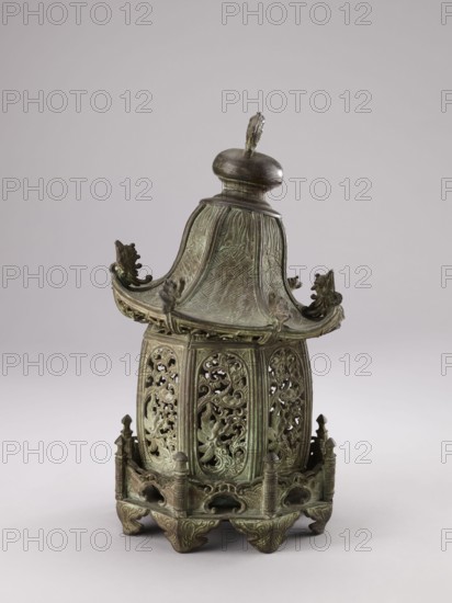 Lantern, ; Chinese, Qing 1644–1911, 19th century; materials/technique not specified; decorated with fish, arbors, plants garden arbors; height 35.0 cm., An ornate metal vessel with a pagoda-like lid sits against a pale background, showing a greenish patina and areas of darker bronze; the lid has a rounded finial topped by a small loop and curved eaves with decorative animal head terminals, and the sloping surfaces display a textured, crosshatched pattern. The body beneath the roof is cylindrical with several vertically oriented pierced panels featuring intricate openwork of scrolling foliage and stylized bird or leaf motifs, all in the same green and dark bronze tones. The base is raised on carved feet with a pierced apron and small columnar posts at the corners, matching the vessel’s overall antique metal coloration and detailed surface ornamentation.
